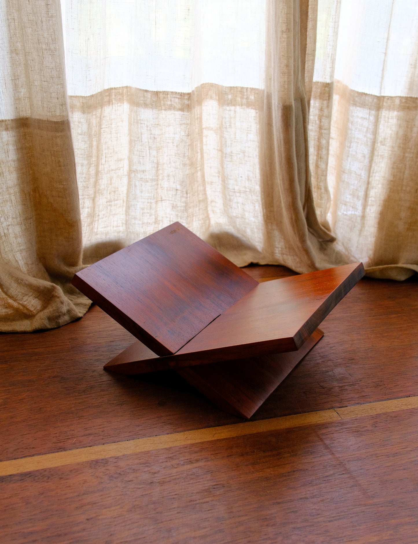Wooden book stand on a wooden floor with light curtains in the background