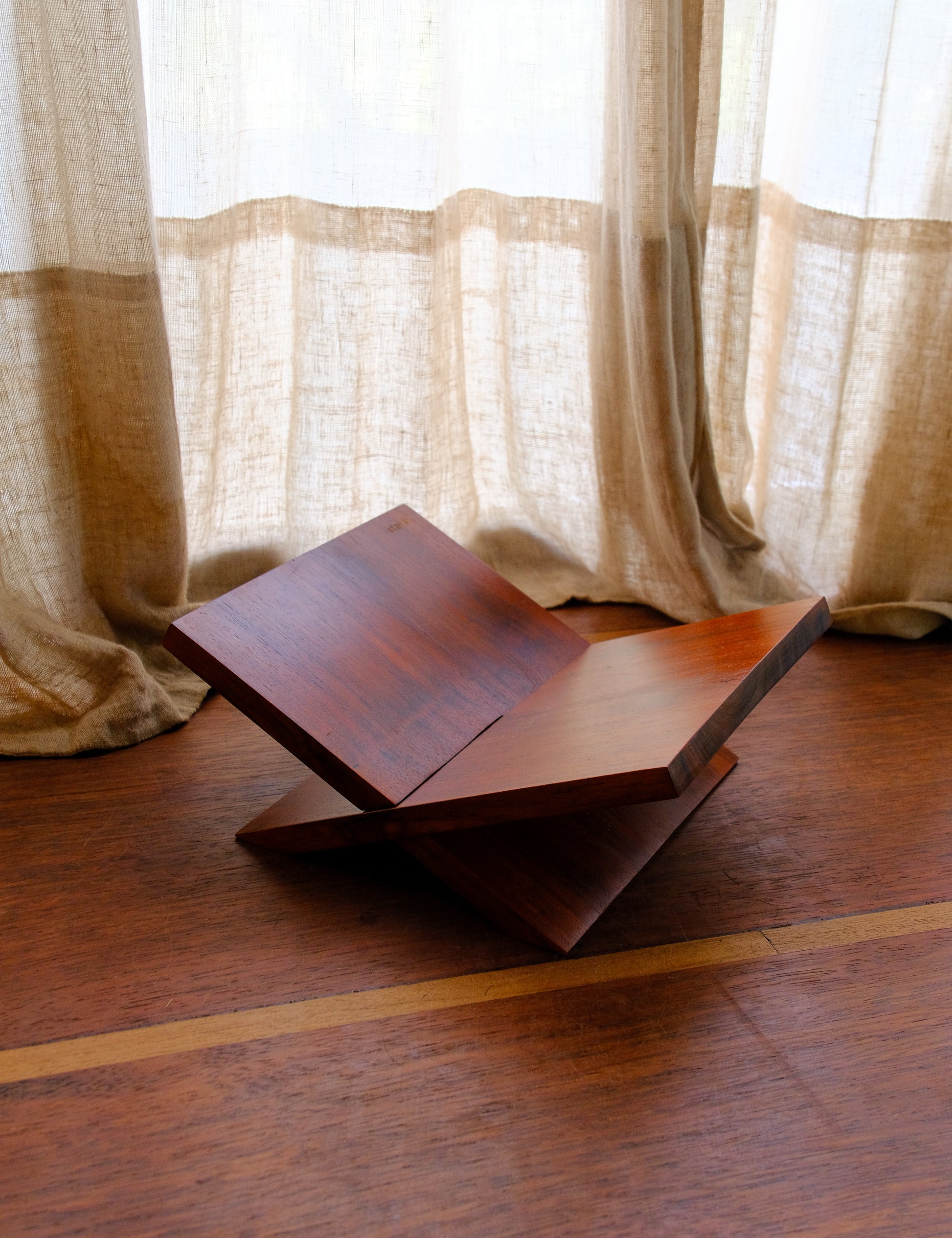 Wooden book stand on a wooden floor with light curtains in the background